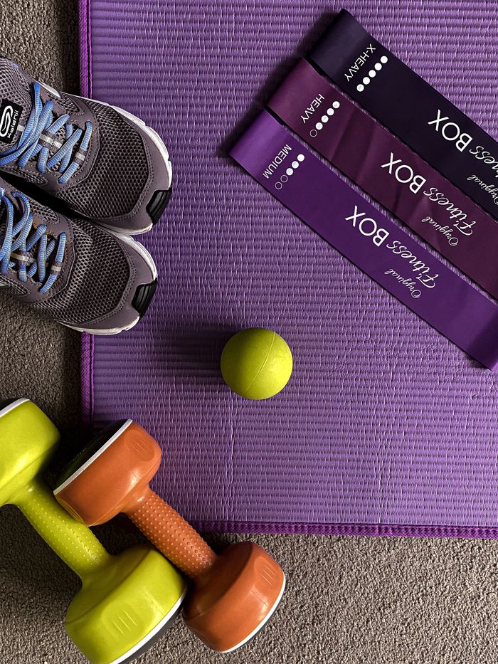 Flat lay of gym shoes, resistance bands, dumbbells on a fitness mat.