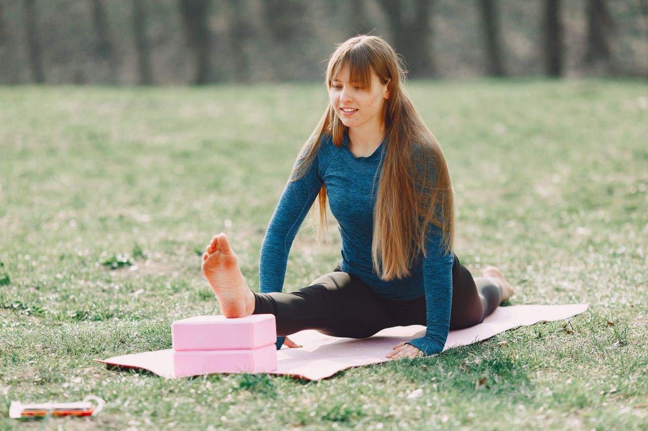 Smiling barefoot sportswoman in sportswear doing yoga leg exercise on sport mat during training on lawn in park adhering to healthy lifestyle while looking down