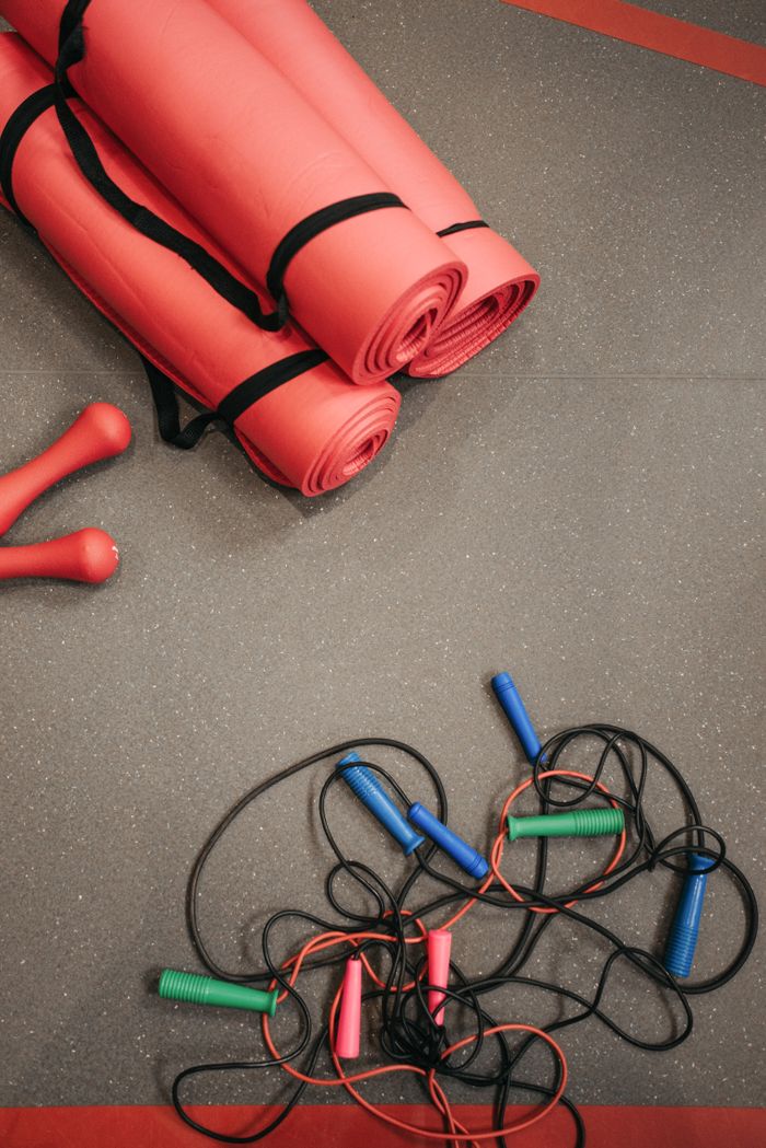 Top view of red yoga mats, jump ropes, and dumbbells on gym floor.