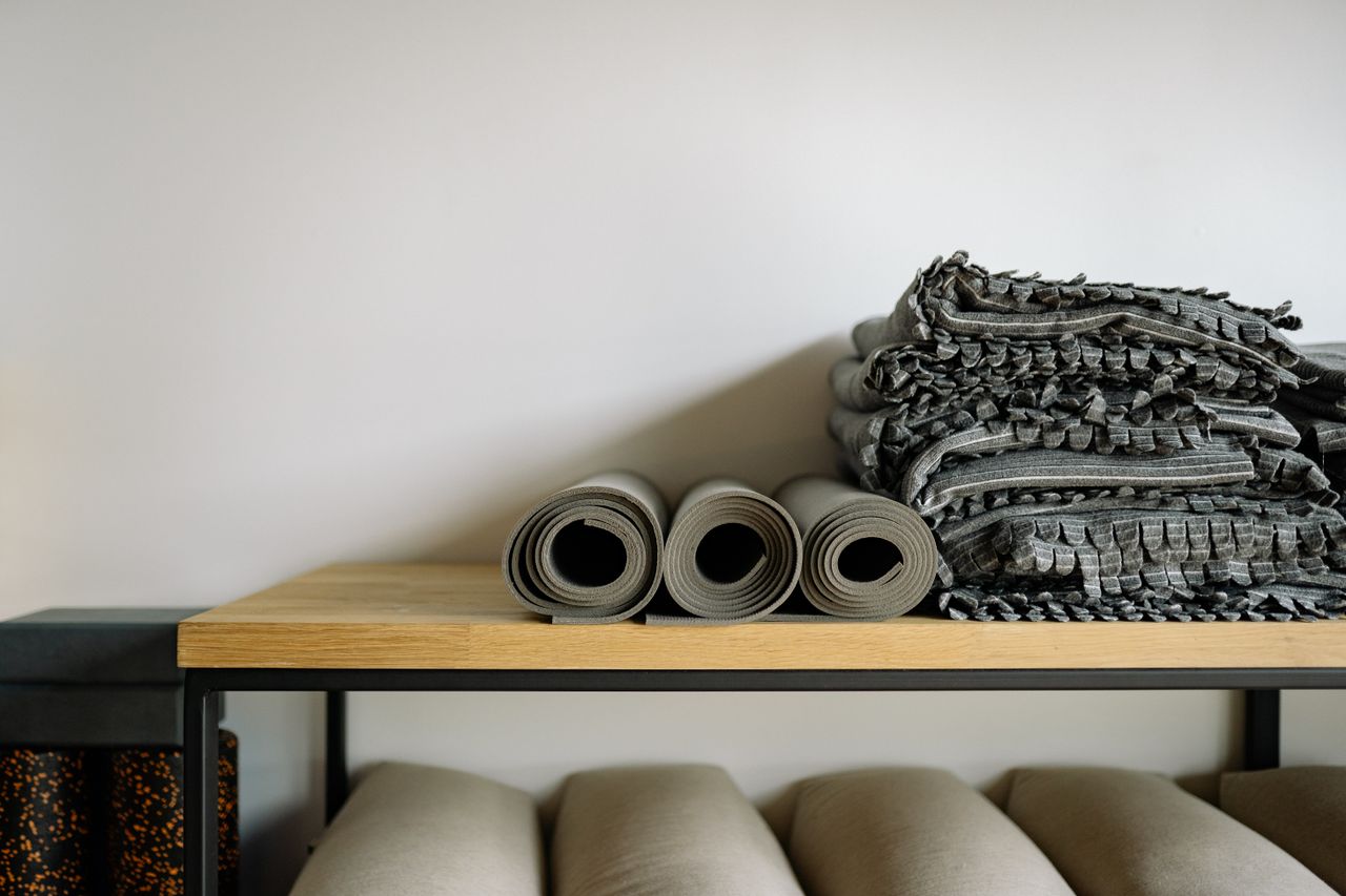 Neatly arranged yoga mats and blankets on a shelf in a serene yoga studio setting.